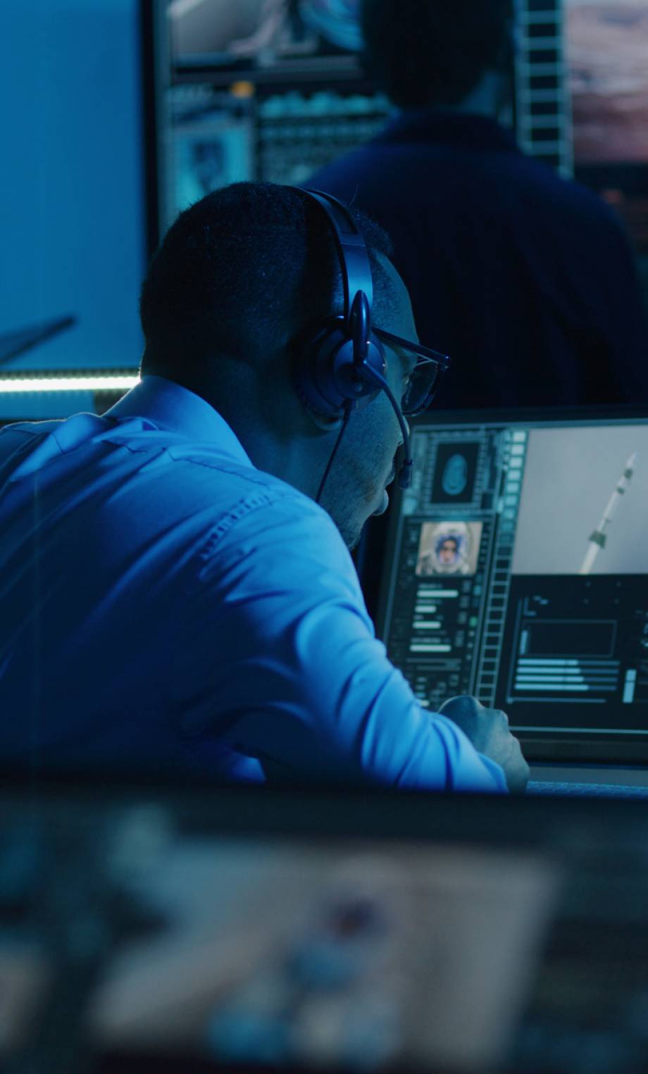 African American flight control employee monitors space mission on multi-monitor computer in mission control center. Team watch successful spacecraft lift off on big digital screen. Space exploration.